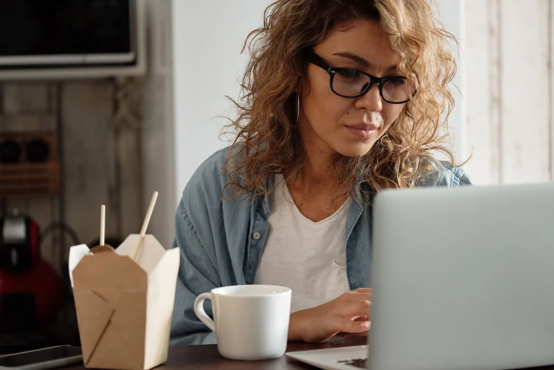 Frau in offenem Jeanshemd und weißem T-Shirt an einem Laptop.