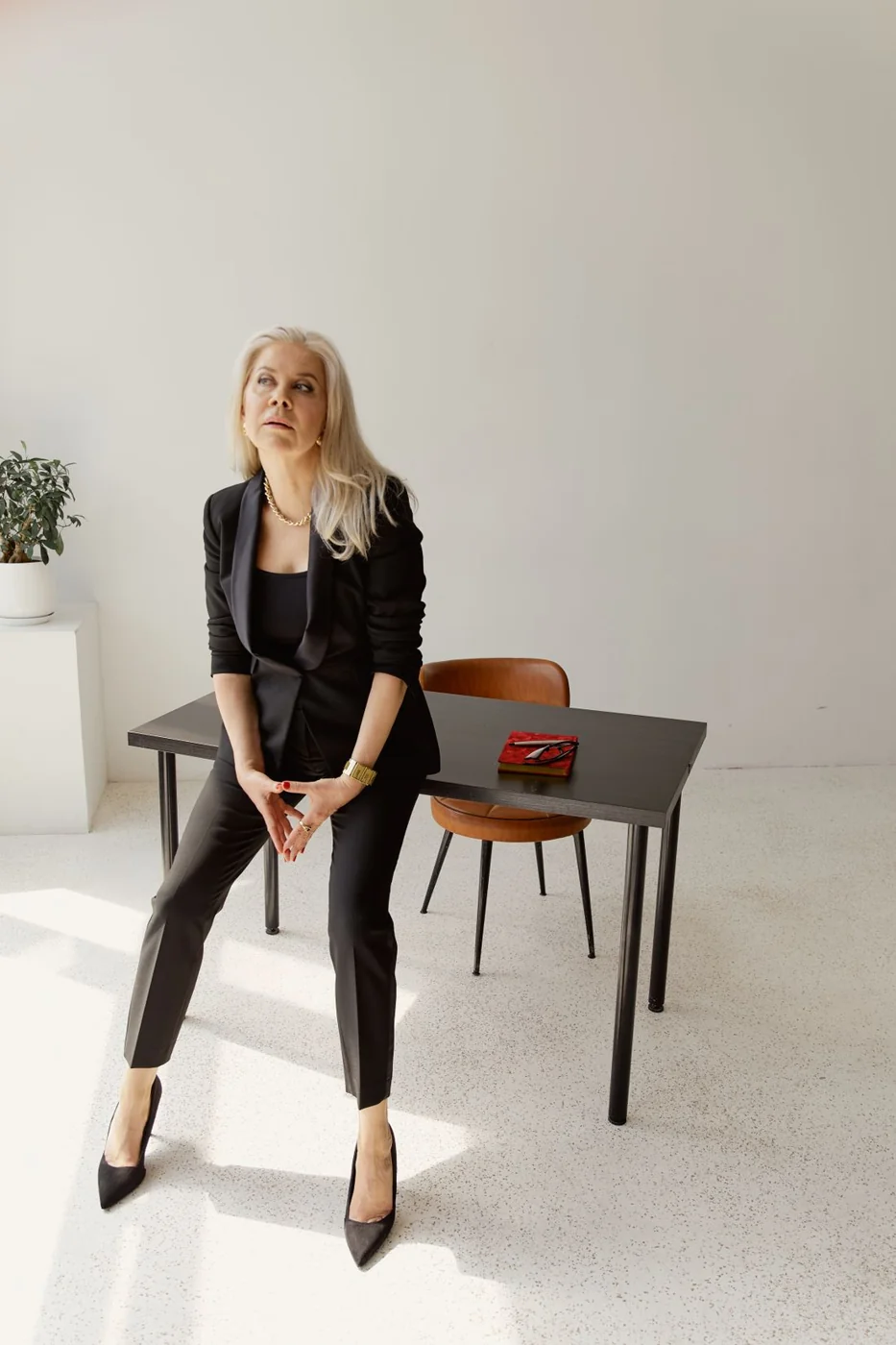 Frau in schwarzem Blazer und Hose auf einem Stuhl im Büro.