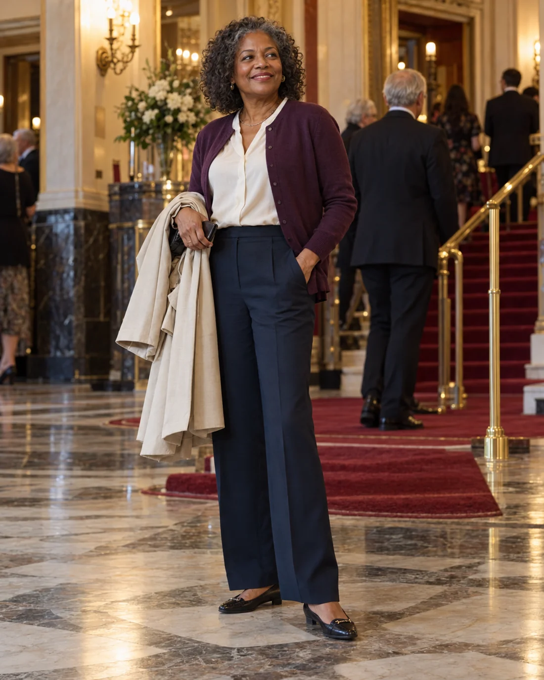 Frau in dunkler Hose und heller Bluse mit Mantel im Theaterfoyer.