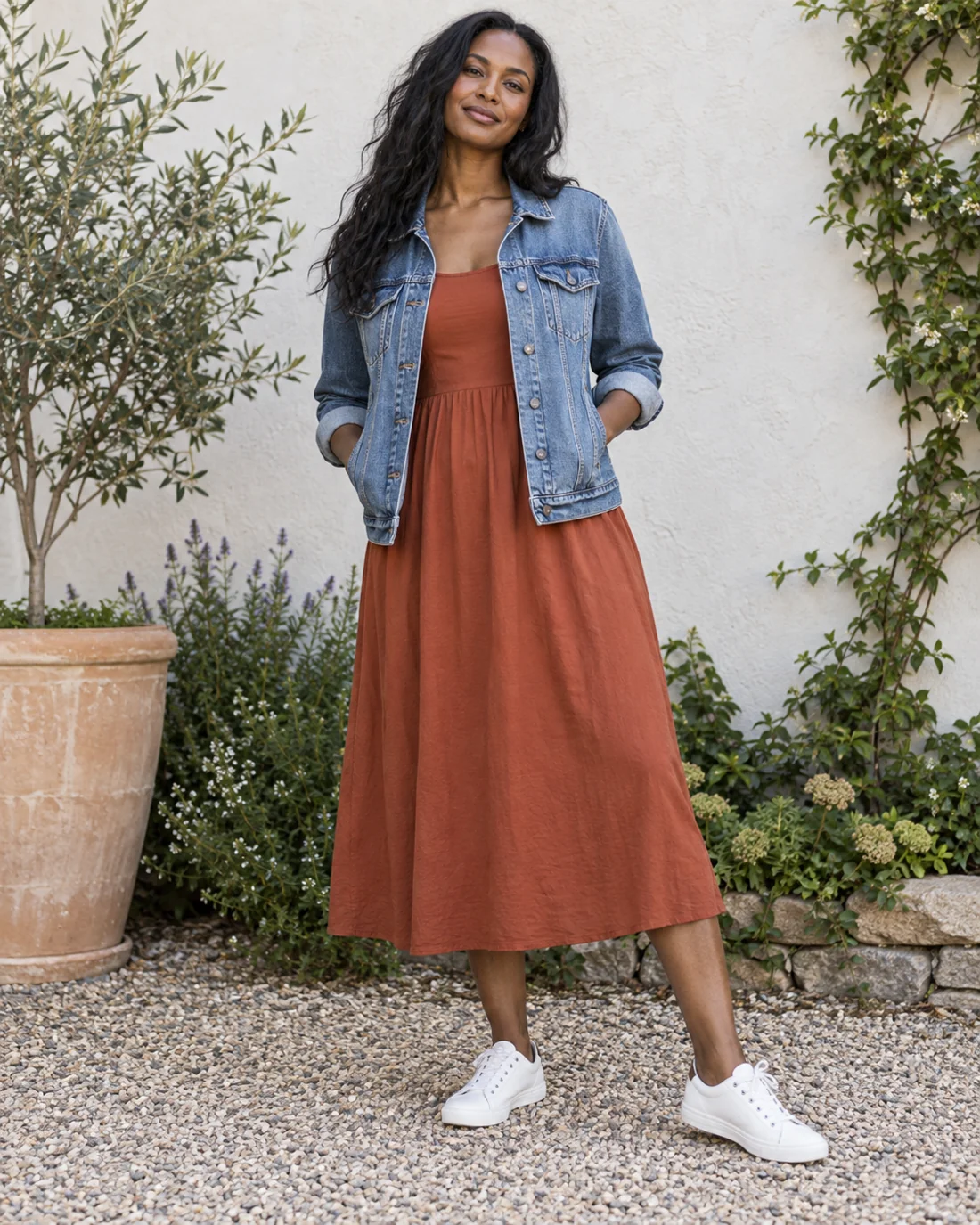 Blaue Jeansjacke über einem rostfarbenen Kleid mit Turnschuhen.