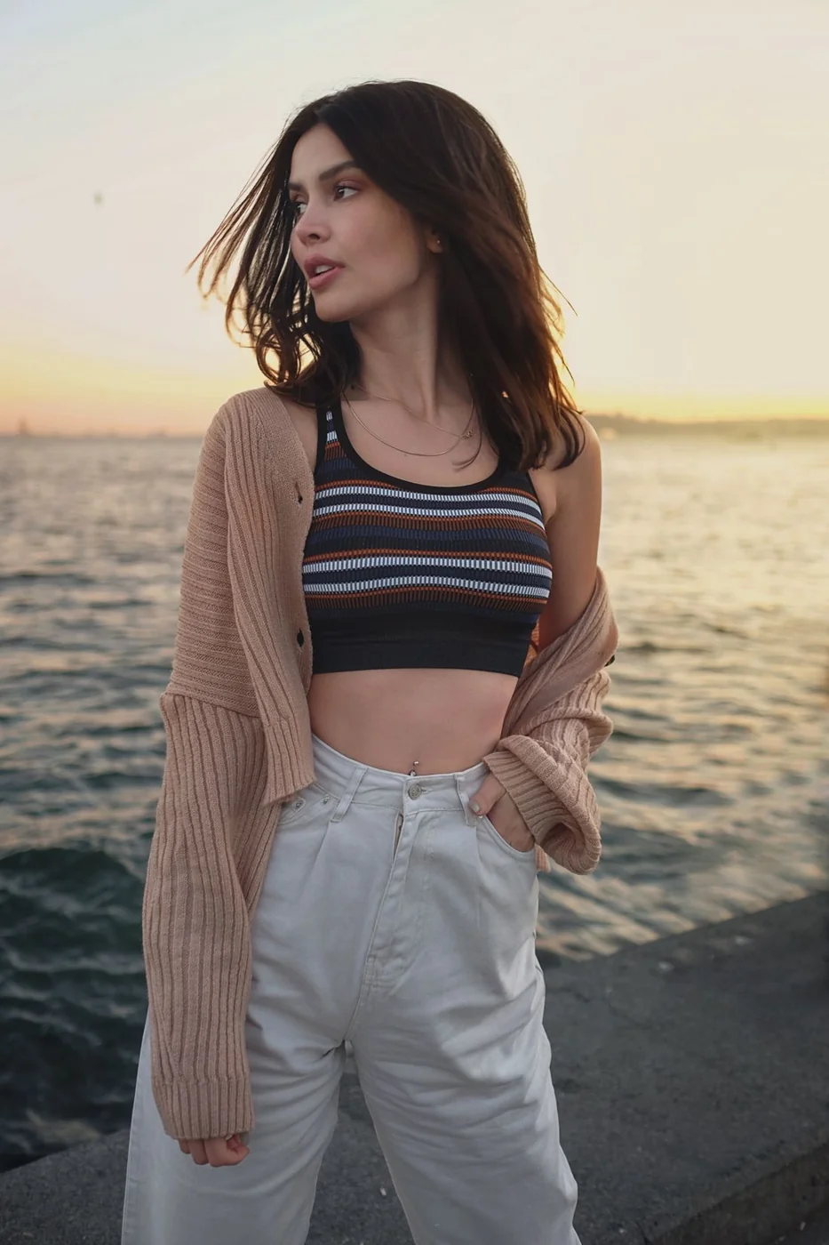 Frau in Strickjacke und gestreiftem Top am Meer.