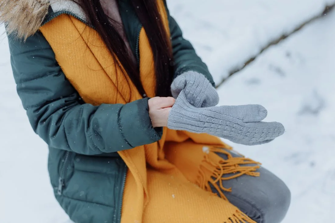 Graue Handschuhe, gelber Schal und grüne Winterjacke.